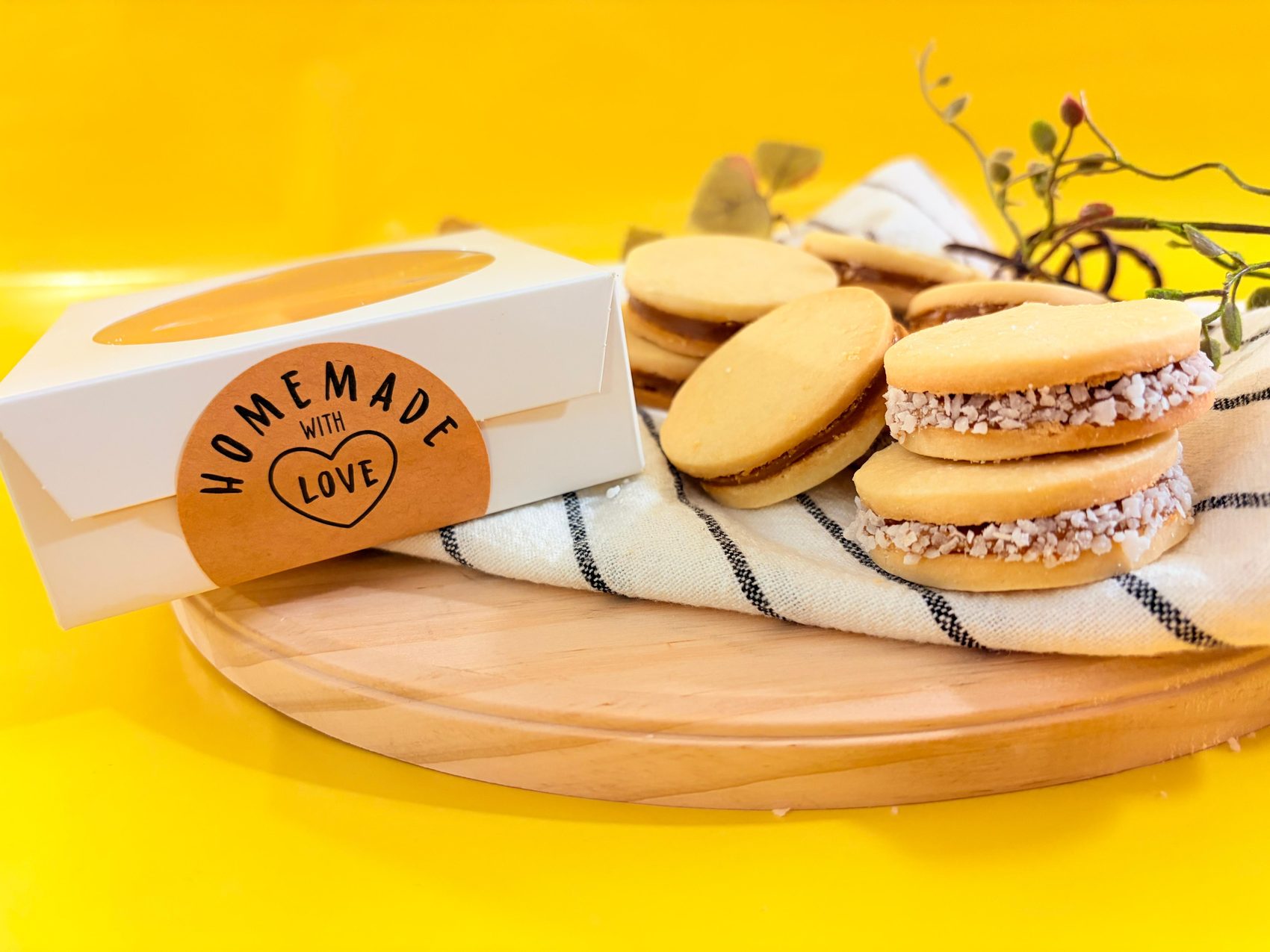 A box of Nina's Bakery alfajores next to a stack of alfajores on a kitchen towel